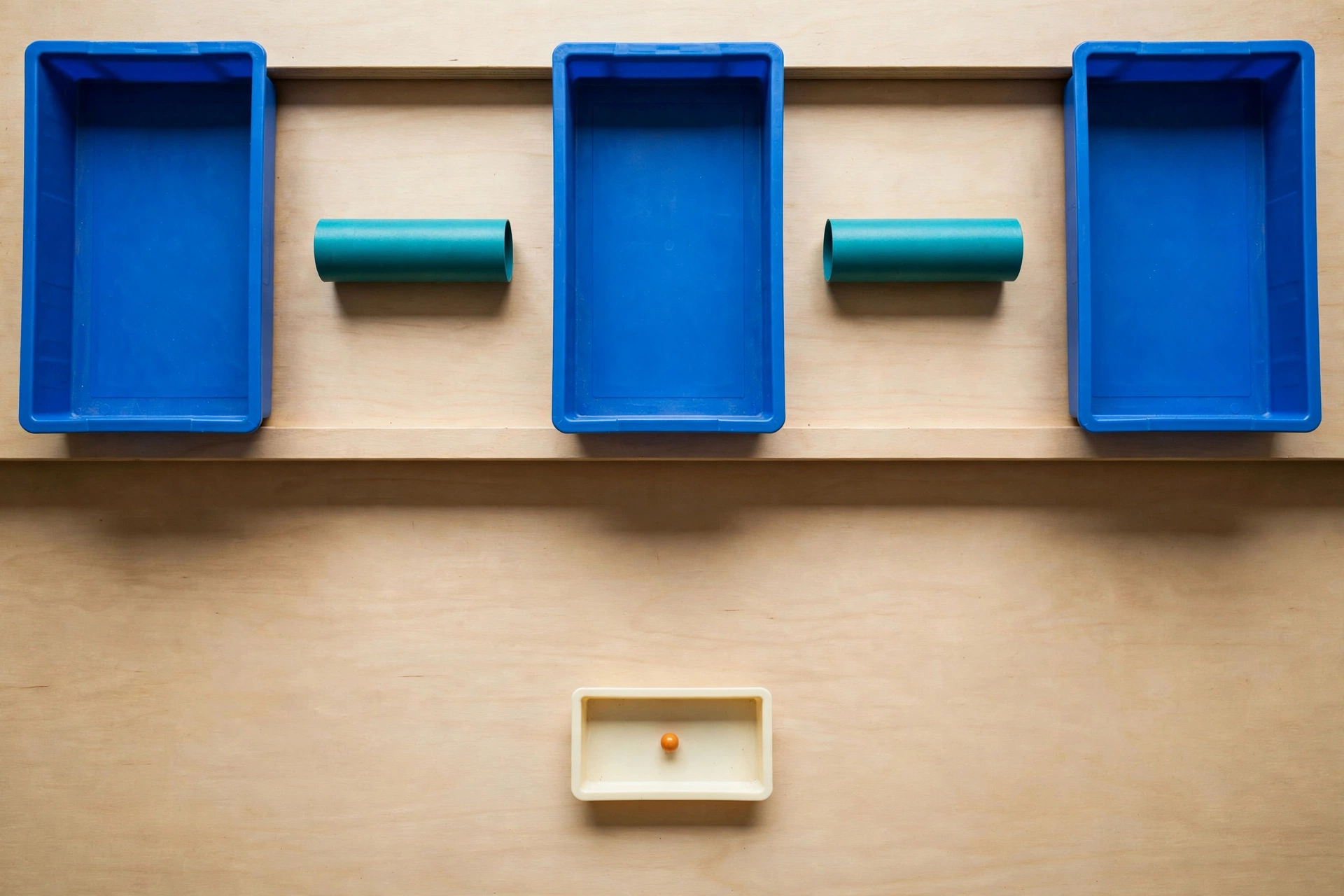 Three blue trays and two teal cylinders are arranged on a wooden surface, with a smaller ivory tray containing an orange bead below.
