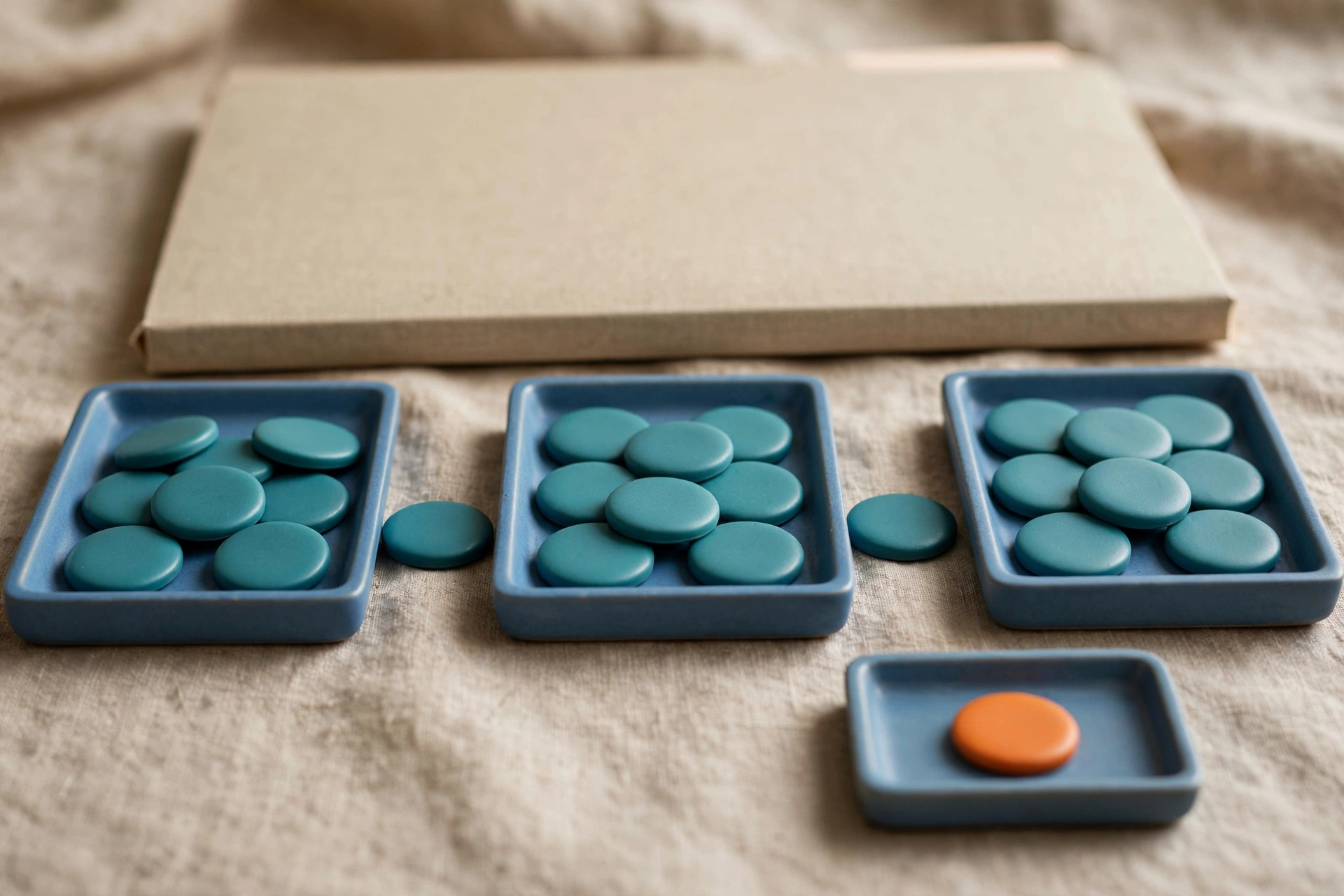Three blue trays with teal tokens are arranged left to right, with a separate tray holding one orange token, and a closed folder behind.