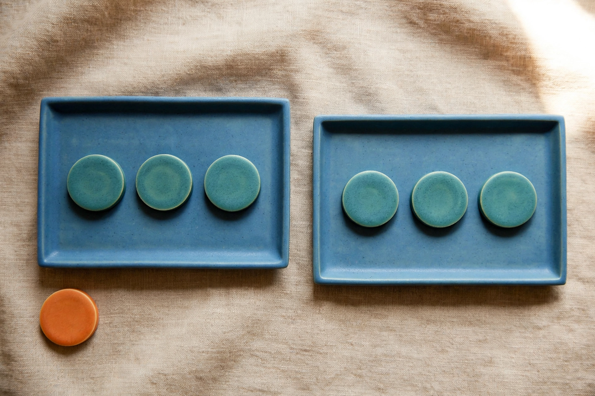 Two blue trays with teal tokens and an orange token beside them on a textured surface.