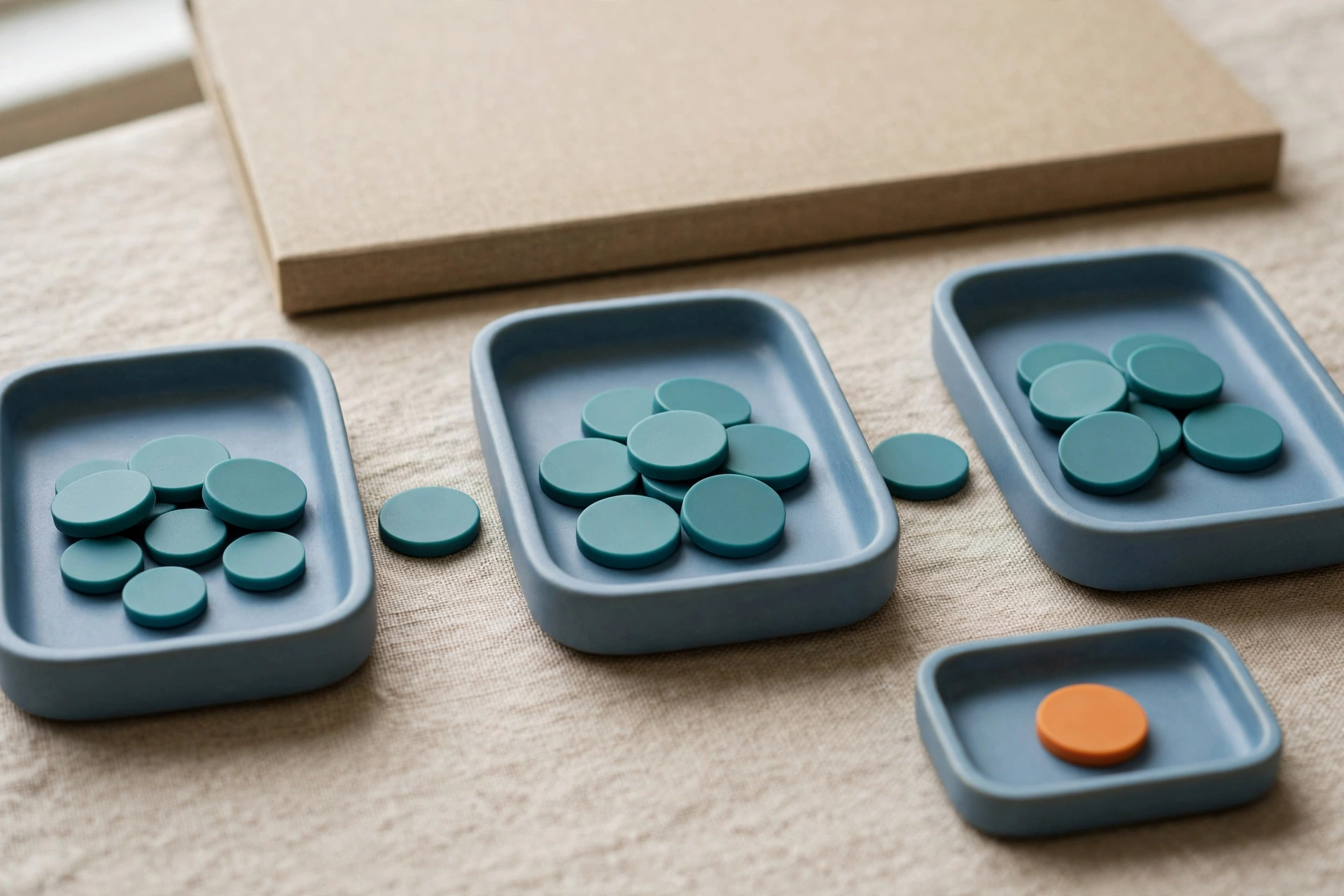 Three blue trays with teal tokens are arranged left to right, with a separate small blue tray holding one orange token.