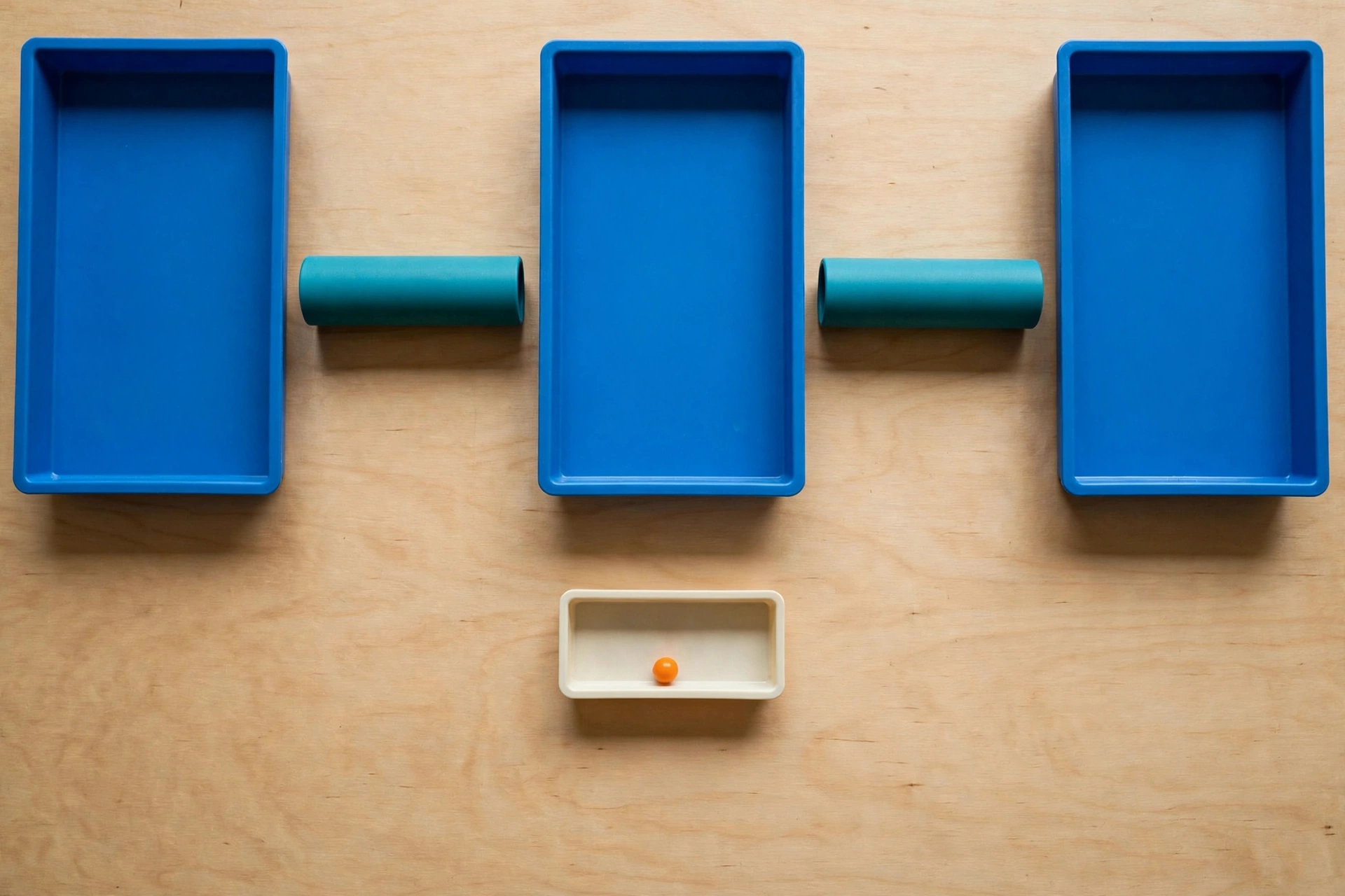 Three blue rectangular trays are arranged horizontally with two teal cylinders between them, and a small ivory tray with an orange bead below.